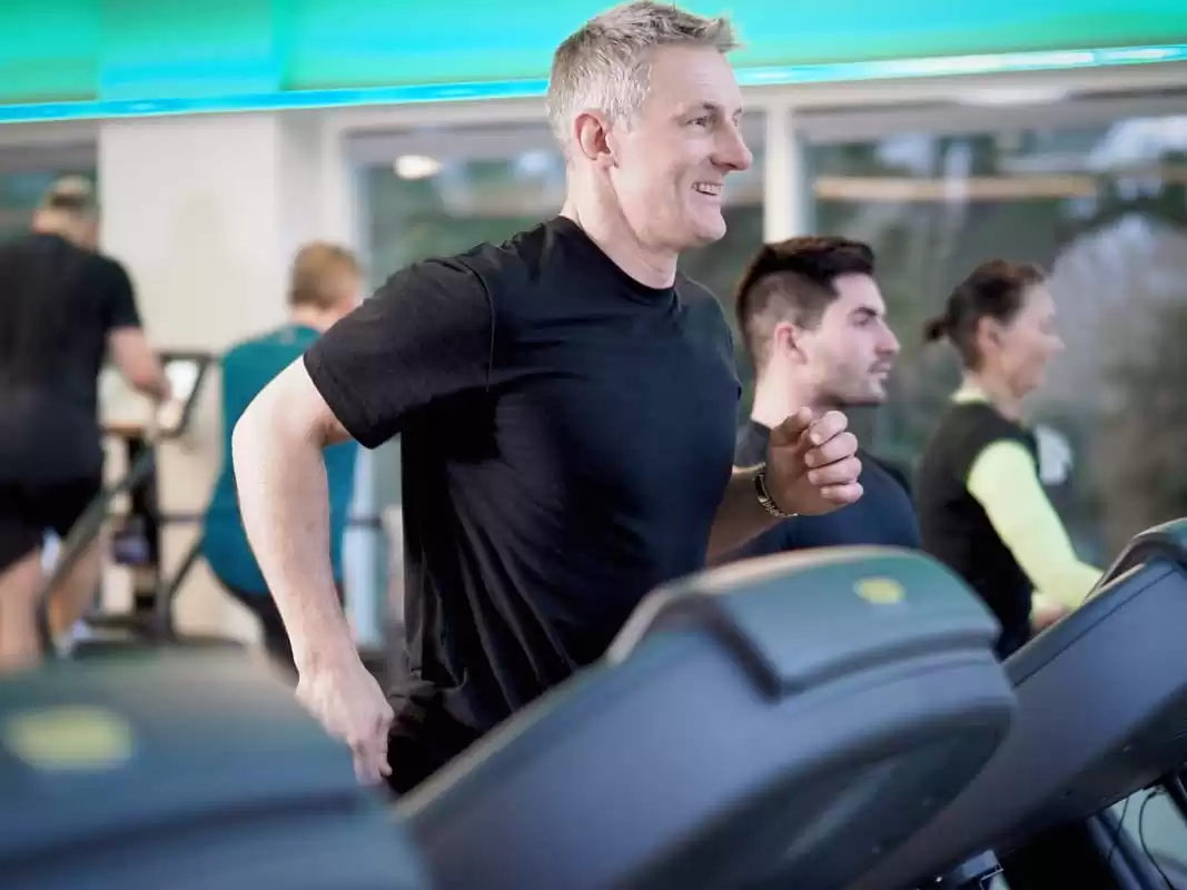 An athletic man runs energetically on the treadmill within the Lensbury gym in Teddington, a members club where leisure centre classes are available to participate in. The health and fitness centre is open 6:00-22:00 Monday to Thursday, 6:00-21:00 Friday and 7:00-20:00 on weekends.