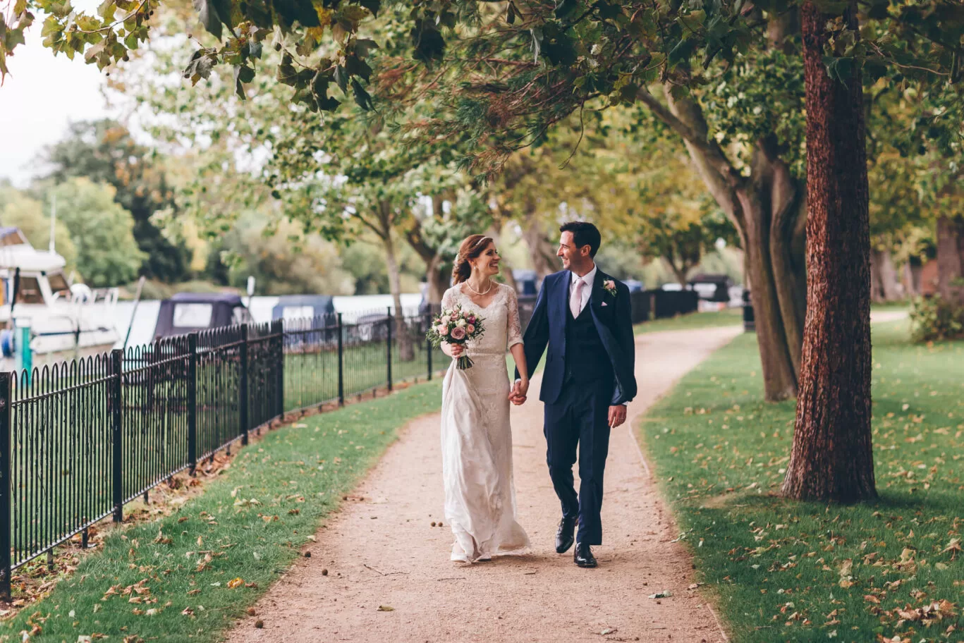 Married couple walking along the river after wedding at The Lensbury a riverside wedding and reception package venue near me