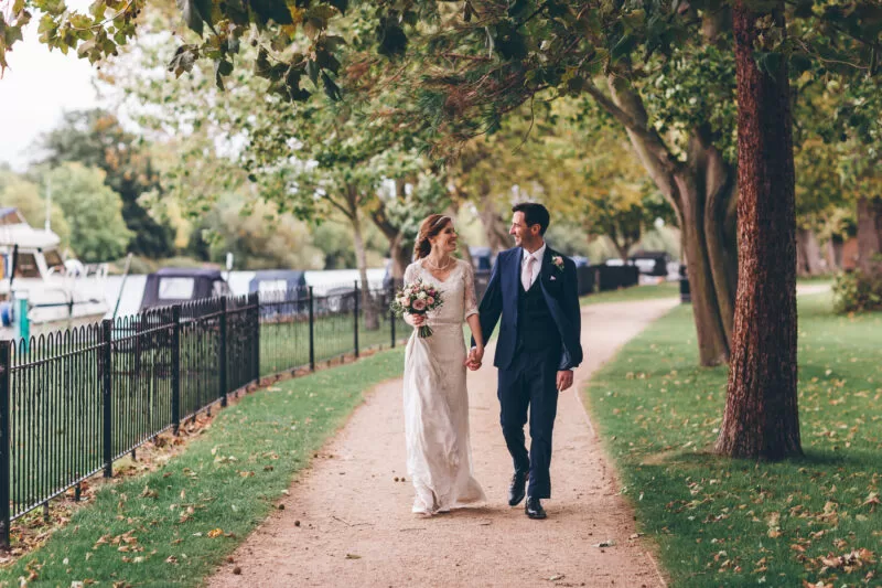 Married couple walking along the river after wedding at The Lensbury a riverside wedding and reception package venue near me