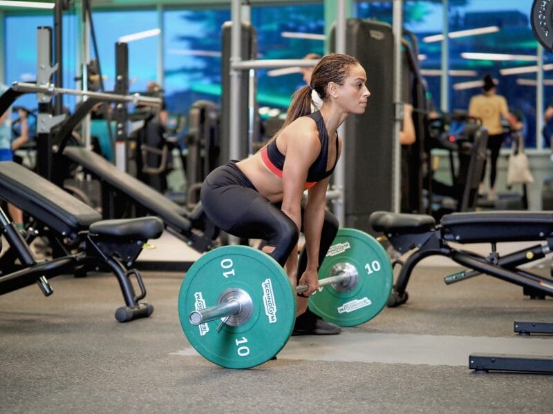 Athletic young woman lifting a heavy weighted bar within the The Lensbury gym, a venue offering leisure centre classes and workouts in Teddington.