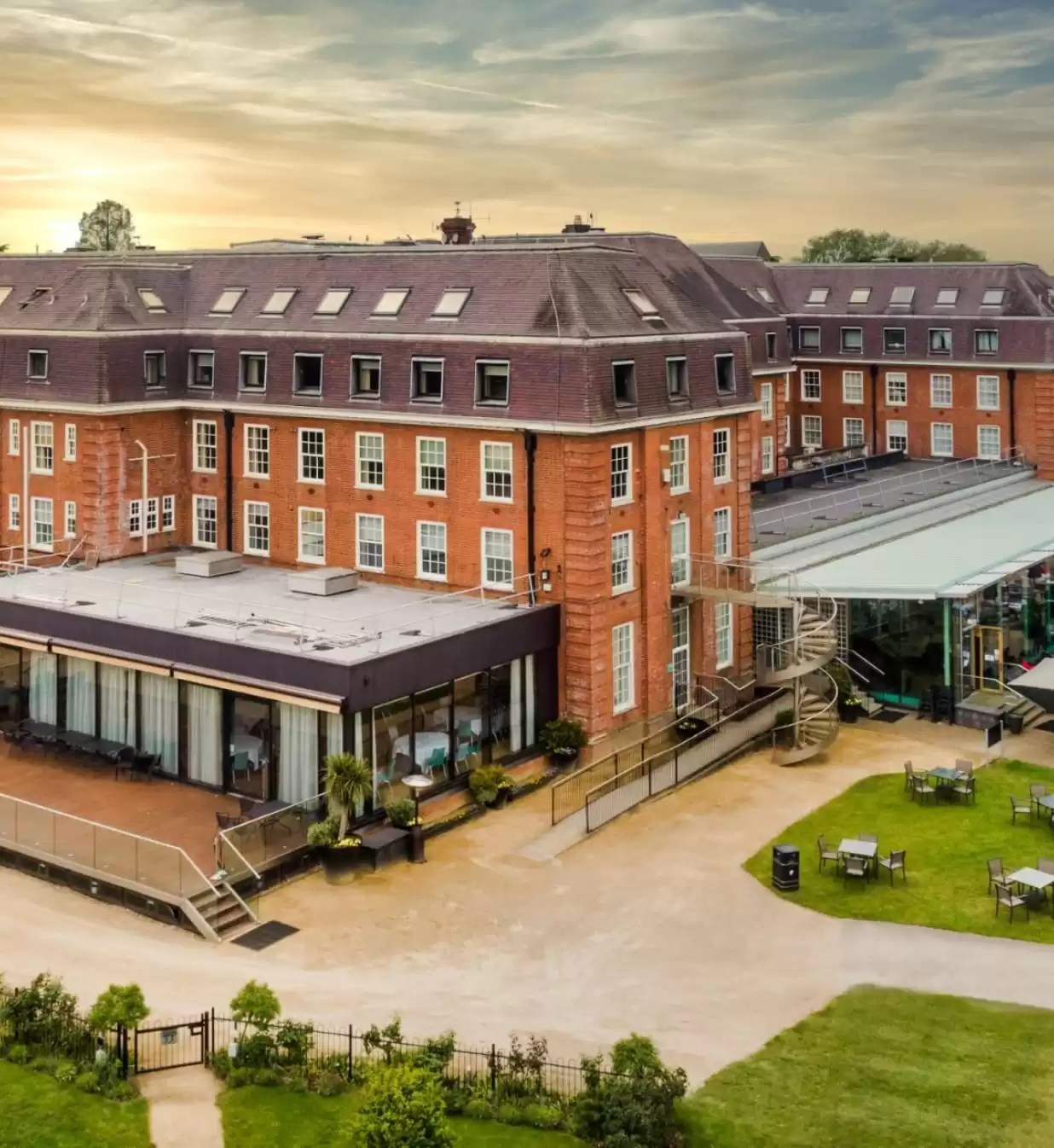 High shot of the external Lensbury grounds, with the main club building in the centre of the shot and the sun beginning to set in the background